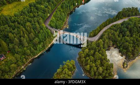 Two arched stone viaducts span deep blue-green water between dense coniferous forest and rocky shoreline. Stock Photo