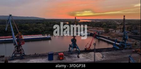 Aerial view of the Danube Port and industrial cranes with cargo barges on the Danube river at sunset in Pancevo, Serbia. Stock Photo