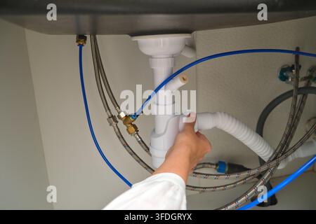 Plumber installing drain pipe under kitchen sink. Siphon connection with water supply hoses and fittings. New kitchen installation, home plumbing repa Stock Photo