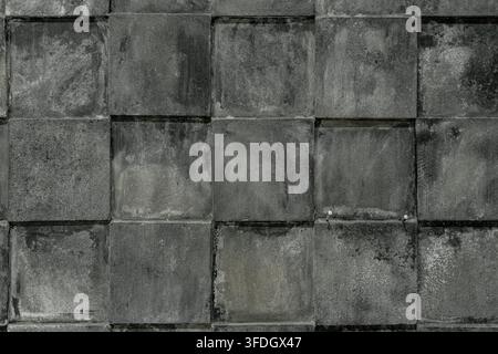 Close up shot of a grey stone wall made of square tiles, featuring natural weathered volcanic rock texture, grid pattern layout. Stock Photo