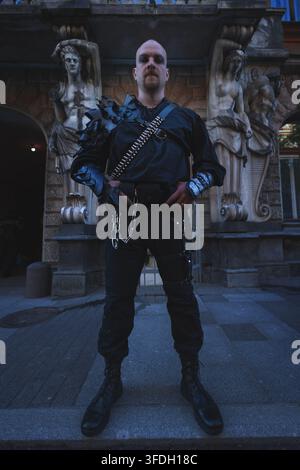 Full length portrait of a man in black leather armor and boots, gothic warrior look. Symmetrical low angle shot between antique stone figures. Stock Photo