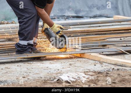 Construction worker in protective gloves cutting steel rebar using an angle grinder on a construction site. Dynamic close-up view of metal processing Stock Photo