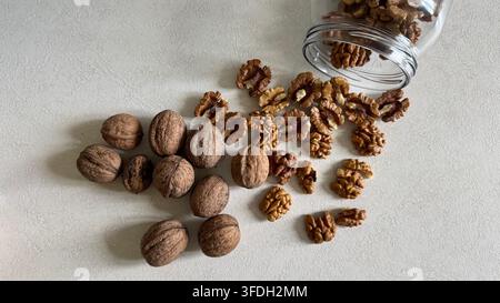 Whole walnuts and walnut kernels arranged as if spilling from a glass jar on a light surface, with generous copy space. Stock Photo