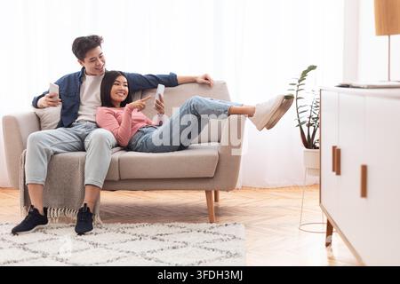 Asian Millennial Couple Using Smartphones Relaxing At Home On Weekend Stock Photo