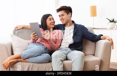 Japanese Spouses Using Tablet Browsing Internet Sitting On Couch Indoor Stock Photo