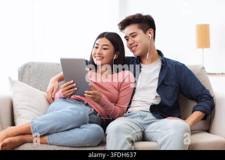 Cheerful Korean Couple Using Digital Tablet Computer Sitting At Home Stock Photo