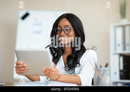 Lovely black business lady in formal wear using tablet pc at workplace Stock Photo