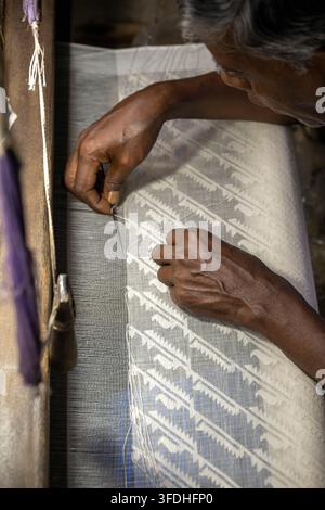 A close-up view of an experienced weaver's hands meticulously working muslin threads on a wooden loom, creating a detailed textile design Stock Photo