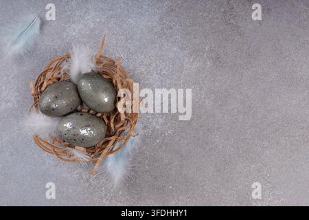 Decorative Easter eggs with silver speckled texture in wicker nest with feathers on gray textured background spring holiday design with copy space Stock Photo