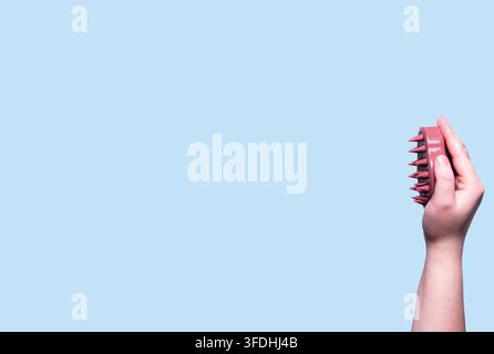 Pink scalp massager brush for hair treatment and care in human hand on blue background Stock Photo
