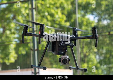 A black military reconnaissance drone flies in front of green trees. Stock Photo