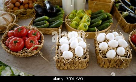 Fresh vegetables and eggs in woven baskets on rustic table Stock Photo