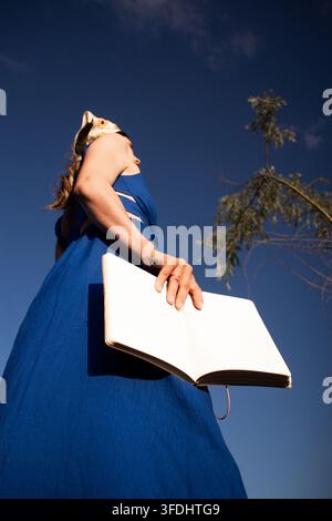 Woman in bright blue dress holding book in hands at very low angle ...