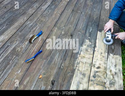 Person sands wooden deck with electric sander. Tools lie nearby on weathered planks Stock Photo