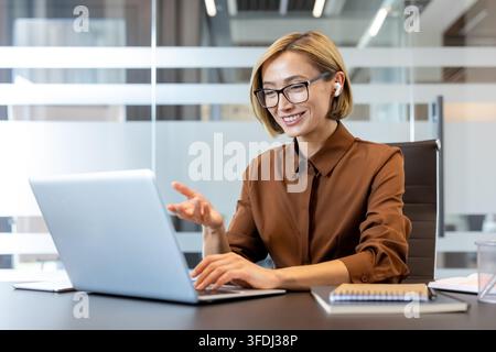Professional businesswoman working at her desk, having a virtual meeting on a laptop and communicating with colleagues, showcasing modern remote work and corporate connection Stock Photo