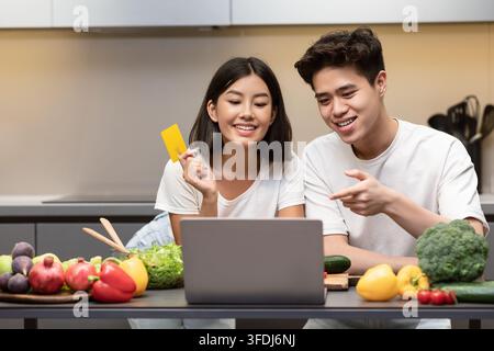 Couple Doing Online Grocery Shopping On Laptop Standing In Kitchen Stock Photo