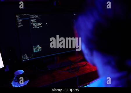 Person programming code on computer screen in dark room, representing cybersecurity, hacking, and software development Stock Photo