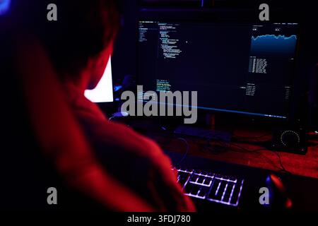 Hacker working in a dark room, typing code on a backlit keyboard, creating software or breaking into systems Stock Photo