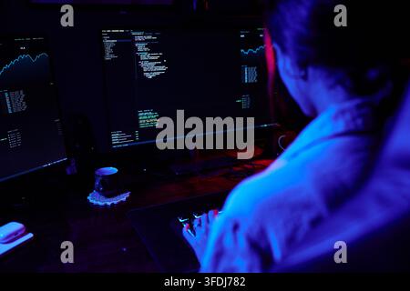 Hacker or programmer writing code on multiple computer monitors, highlighting cybersecurity, technology, and data security concepts Stock Photo