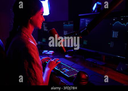 Young woman working or gaming at night, illuminated by blue and red neon lights, showing cyber and technology concepts Stock Photo