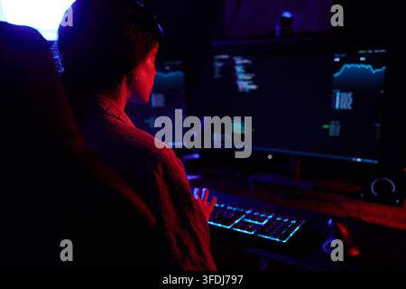 Woman programmer working on computer with code and data on screens, illuminated by red and blue neon light Stock Photo