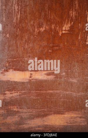 A detailed vertical close-up photograph of an old brown rusted metal surface featuring distressed paint strokes and heavy corrosion for an industrial Stock Photo