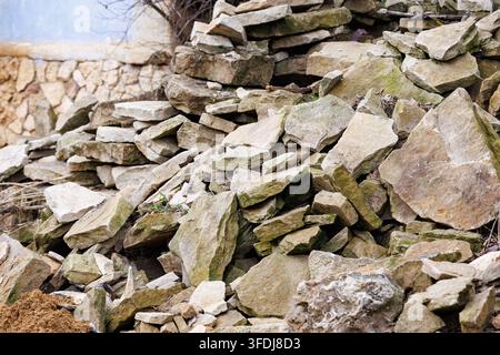 A large pile of natural, rough-hewn flat stones and rock debris lies outdoors on the ground, prepared for use in landscaping, traditional masonry, or Stock Photo