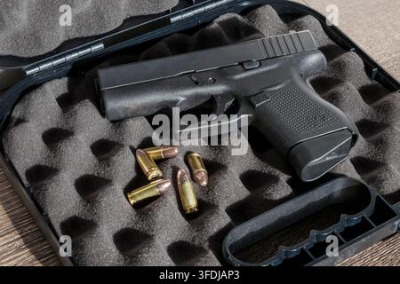 A Glock 43 semi-automatic pistol rests in a foam-lined hard case alongside four loose 9mm cartridges, showcasing the firearm and its ammunition. Stock Photo
