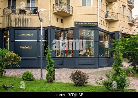 Batumi, Georgia - May 20, 2026: Exterior view of StudioArt gallery facade, display windows with artworks, sidewalk, green plants in foreground. Stock Photo