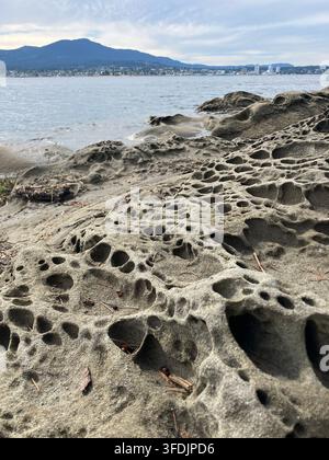 Unique honeycomb sandstone rock formations along a coastal shore at Jack Point and Briggs Park with Nanaimo city skyline across the water. Stock Photo