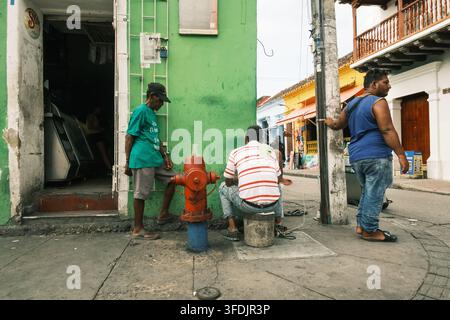 Cartagena, Colombia - 05 July 2023: View of men relaxing on a street corner next to a red fire hydrant in the historic city center. Stock Photo