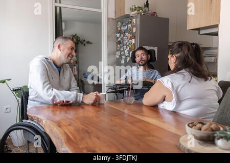 Two men with disabilities and a Personal assistant enjoying talking together and sharing experiences in the home environment. Stock Photo