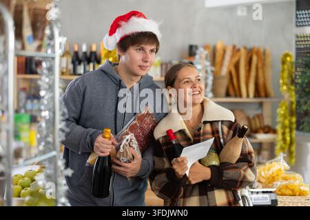 Young couple chooses products at grocery store from a pre-made list for Christmas or New Year celebrations Stock Photo