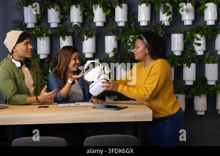 Diverse coworkers examining white VR headset while reviewing tablet and documents at office Stock Photo