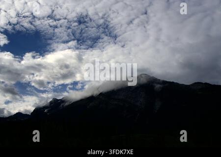 Dramatic Contrast of a Dark Mountain Silhouette Capped with Whispering White Clouds Under a Vast Blue Sky Filled with Textured Cumulus Clouds Stock Photo