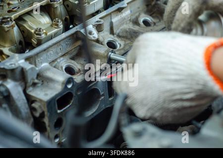 Mechanic wearing protective gloves works on a car engine focusing on internal components and mechanics for repair or maintenance Stock Photo