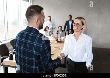 Businessman Shaking Hands With Businesswoman During Corporate Meeting In Office Stock Photo