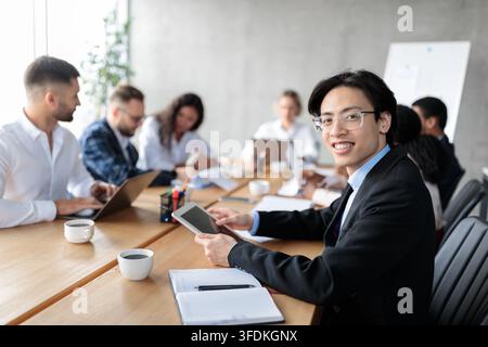 Happy Asian Businessman Using Tablet Sitting With Colleagues In Office Stock Photo