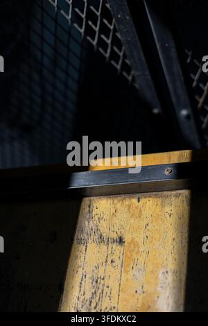 Morning Light Through Perforated Steel Gate, a photograph capturing sunlight filtering through a roof, casting striking shadows on a textured steel ga Stock Photo