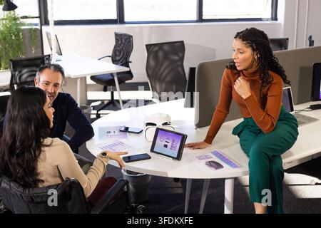 Diverse coworkers discussing project at table using tablet and printed graphs at modern office Stock Photo