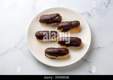 Delicious Chocolate Glazed Eclairs with Cream Filling on a White Plate Stock Photo