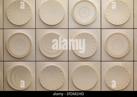 Cream Geometric Tile Pattern with Circular Reliefs. Cream square tiles with raised circular motifs featuring waves, rings, scales, and concentric Stock Photo