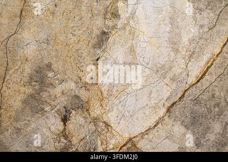 Beige and Gray Marble Stone Texture. Close-up of beige and gray marble with natural gold veining, fine cracks, mottled mineral patterns, and weathered Stock Photo