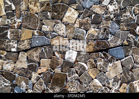 Brown and Gray Natural Stone Mosaic Texture. Irregular polished stone mosaic pieces in brown, gray, beige, and white with natural veining and varied Stock Photo