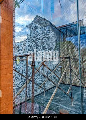 Glass reflects textured wall and rusty railing. Modern urban architecture meets industrial decay Stock Photo