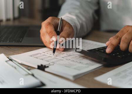 Businessman pointing at printed financial documents with pen while using calculator for corporate budgeting, accounting review, revenue analysis, expe Stock Photo