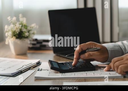 Businessman reviewing financial documents with calculator, pen, laptop for corporate budgeting, accounting analysis, revenue planning, expense control Stock Photo