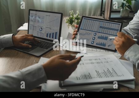 Two businessmen discussing spreadsheet tables and charts on laptop and tablet during business meeting for data analysis, financial reporting and perfo Stock Photo