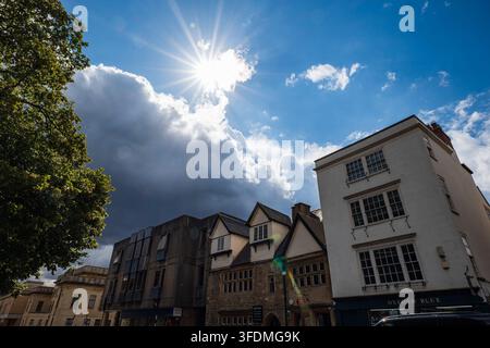 Oxford, Oxfordshire, England, August 20, 2026. Low angle shot of shopfront facades along St Aldate's street with a sun star burst and clouds. Stock Photo