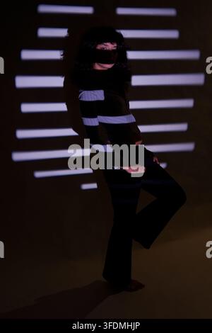 Woman standing in dark room with light lines projected onto her face and clothes Stock Photo